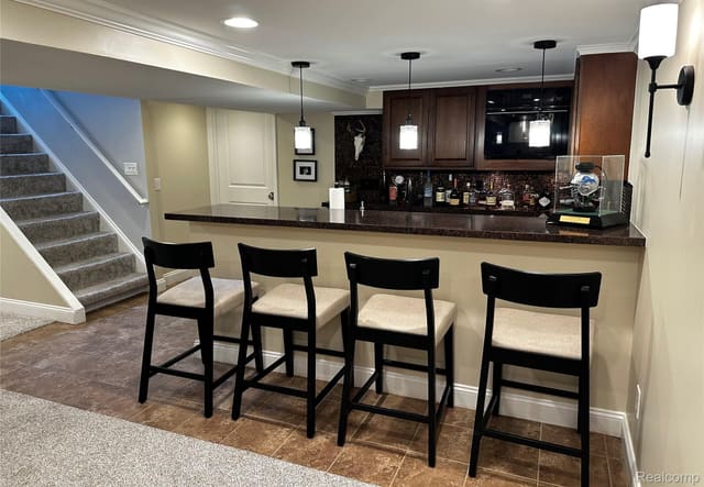 Wet bar with bar-stool seating beside the basement stairs
